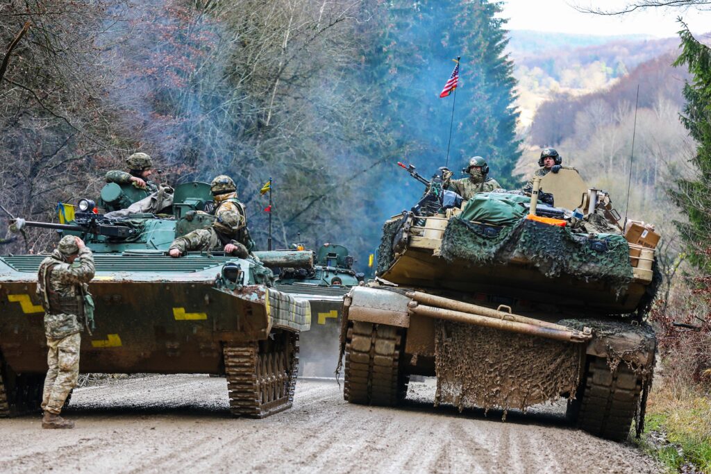 Photograph shows an American and Ukrainian tank passing one another on a road during a NATO training mission on the edge of a German forest.